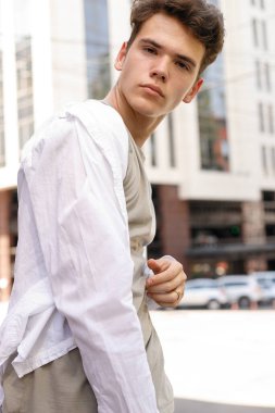 Beyaz gömlekli ve gri pantolonlu şık saç kesimi olan bir erkek model. Modayı takip eden saç stili modern bir iş merkezine yakın. Bir yaz gününde sokakta çekici bir adam..