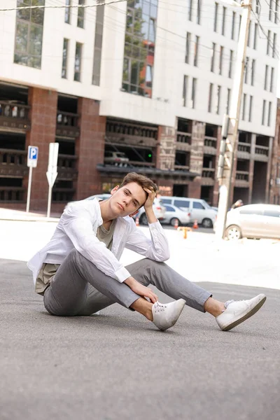 guy model with a stylish haircut posing outdoors in a white shirt and gray trousers. trendy hairstyle rests near a modern business center. Attractive guy in the street on a summer day.