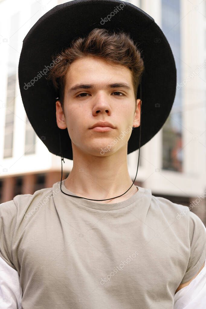 portrait of a trendy young man in the city. close-up portrait guy model in a black hat on the street