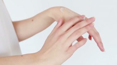 Güzellik, insanlar ve sağlık konsepti - el kremi süren genç bir kadının temiz ve bakımlı elleri, beyaz bir arka planda cilt bakımı. Yakın plan. Şehvetli kadın cildini nemlendirir. 4K, Ağır çekim