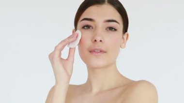 Güzel genç bir kadının çıplak yüzünü pamukla silerken ve kameraya bakarken yakın plan çekimleri. Deri tedavisi konsepti videosu, tene dokunmak, deri konsepti videosu. 4K, Ağır çekim