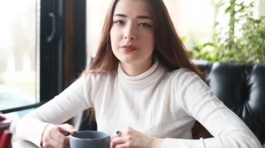 Kafede güzel bir kadının aletleriyle sabah çayı. Çekici bir bayanın hoş yüzünü kapayın ve bardaktan sıcak bir içecek için. Kahve ya da kafede çay içen gülümseyen kadın olumlu duygular besliyor. 4k