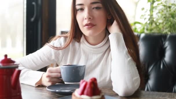 カフェで美しい女性のガジェットと朝のお茶 カップから魅力的な女性の飲み物の快適な顔を閉じます 肯定的な感情を持つカフェでコーヒーやお茶を楽しむ笑顔の女性 — ストック動画