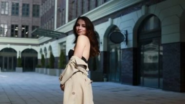 Bej yağmurluklu, baştan çıkarıcı genç bir kadın. Şehre bahar günü poz veriyor. Şık bahar kıyafetleriyle esmer model kız şehir arka planında poz veriyor. Siyah seksi iç çamaşırlı bir model.