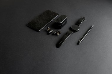 Tek renkli arka planda erkek güzelliği için aksesuarlar. Siyah kalem, siyah akıllı saat, akıllı telefon ve karanlık arka planda kablosuz kulaklık. Yukarıdan bak. Minimalist siyah eğilim 2020.