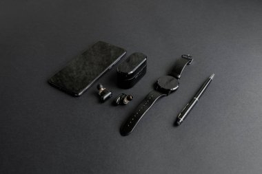 Tek renkli arka planda erkek güzelliği için aksesuarlar. Siyah kalem, siyah akıllı saat, akıllı telefon ve karanlık arka planda kablosuz kulaklık. Yukarıdan bak. Minimalist siyah eğilim 2020.