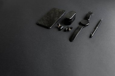 Tek renkli arka planda erkek güzelliği için aksesuarlar. Siyah kalem, siyah akıllı saat, akıllı telefon ve karanlık arka planda kablosuz kulaklık. Yukarıdan bak. Minimalist siyah eğilim 2020.