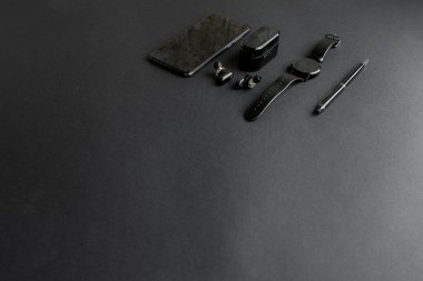 Tek renkli arka planda erkek güzelliği için aksesuarlar. Siyah kalem, siyah akıllı saat, akıllı telefon ve karanlık arka planda kablosuz kulaklık. Yukarıdan bak. Minimalist siyah eğilim 2020.