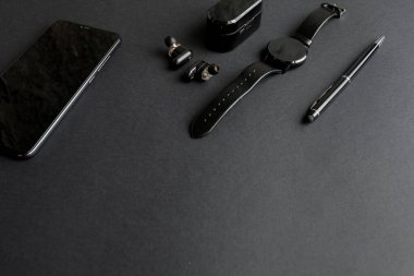 Tek renkli arka planda erkek güzelliği için aksesuarlar. Siyah kalem, siyah akıllı saat, akıllı telefon ve karanlık arka planda kablosuz kulaklık. Yukarıdan bak. Minimalist siyah eğilim 2020.