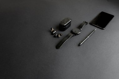 Tek renkli arka planda erkek güzelliği için aksesuarlar. Siyah kalem, siyah akıllı saat, akıllı telefon ve karanlık arka planda kablosuz kulaklık. Yukarıdan bak. Minimalist siyah eğilim 2020.