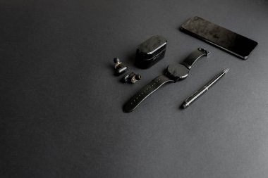 Tek renkli arka planda erkek güzelliği için aksesuarlar. Siyah kalem, siyah akıllı saat, akıllı telefon ve karanlık arka planda kablosuz kulaklık. Yukarıdan bak. Minimalist siyah eğilim 2020.