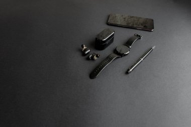 Tek renkli arka planda erkek güzelliği için aksesuarlar. Siyah kalem, siyah akıllı saat, akıllı telefon ve karanlık arka planda kablosuz kulaklık. Yukarıdan bak. Minimalist siyah eğilim 2020.