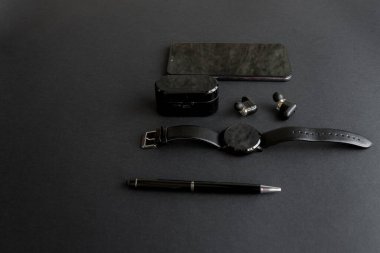 Tek renkli arka planda erkek güzelliği için aksesuarlar. Siyah kalem, siyah akıllı saat, akıllı telefon ve karanlık arka planda kablosuz kulaklık. Yukarıdan bak. Minimalist siyah eğilim 2020.