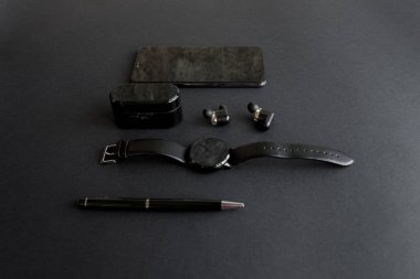 Tek renkli arka planda erkek güzelliği için aksesuarlar. Siyah kalem, siyah akıllı saat, akıllı telefon ve karanlık arka planda kablosuz kulaklık. Yukarıdan bak. Minimalist siyah eğilim 2020.