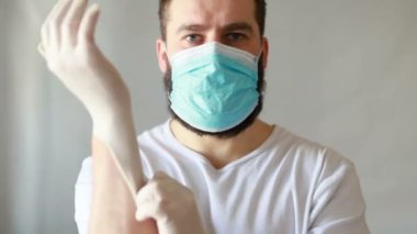 Koruyucu maskeli bir adam öksürüyor. Adam hasta, üşütmüş, öksürüyor. Beyaz koruyucu takım elbiseli beyaz sakallı adam kameraya baktı ve yüzüne tıbbi bir maske taktı. Kapat.