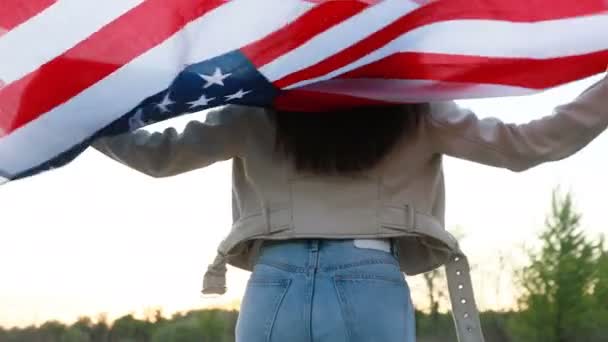 Fiatal nő lengeti az amerikai zászlót, és lassított felvételekkel veszi körbe magát. mint a szabadság, az ifjúság és a függetlenség szimbóluma, fogalom mindörökre fiatal. Mosolyog.