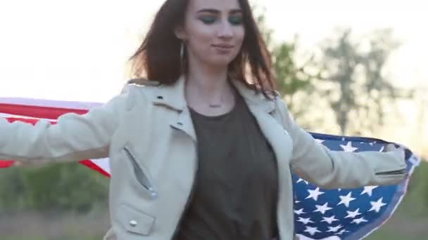 若い女性はアメリカ国旗を振ってゆっくりと動き回る 自由と若さと自立の象徴としての概念は永遠に若いのです 彼女は笑っている — ストック動画