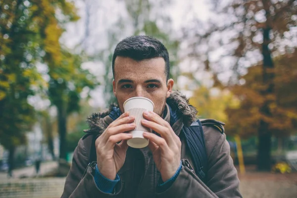 Man in coat holding a cup of coffee latte with milk. Lonely woman stands on  snowy autumn deserted street in the park. — Stock Photo, Image