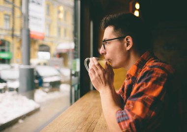 Genç öğrenci restoranda oturuyor ve sıcak bir içecek tadıyor. Kafede çay içen adam.