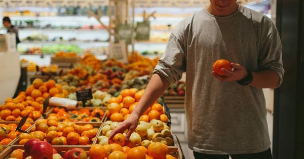 Esto debería estar bien. Guapos hombres jóvenes naranja pimienta y bolsa de compras, mientras que de pie en una tienda de alimentos — Foto de Stock