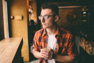 Genç öğrenci restoranda oturuyor ve sıcak bir içecek tadıyor. Kafede çay içen adam.