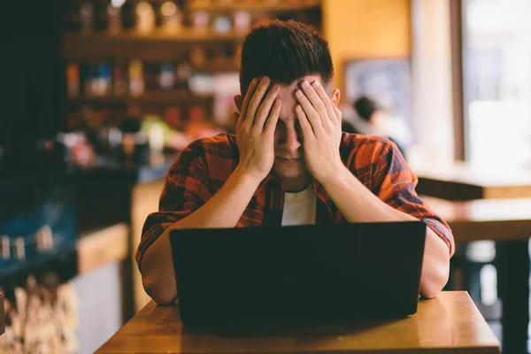 Happy casual man using smartphone and laptop computer in cafe under stress  preparing for exams