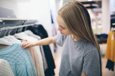 Güzel sarışın bir giyim mağazasından yeni şeyler alıyor. Satıcı butikte çalışıyor.