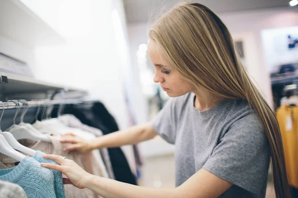 Krásná blondýna kupuje nové věci v obchodě s oblečením. Prodávající pracuje v butiku — Stock fotografie