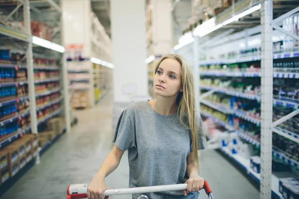 Curious Woman in The Supermarket . Young girl in a market store with  shopping thinking what to buy
