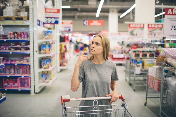 Una donna curiosa al supermercato. Ragazza in un negozio di mercato con lo shopping pensando a cosa comprare — Foto Stock