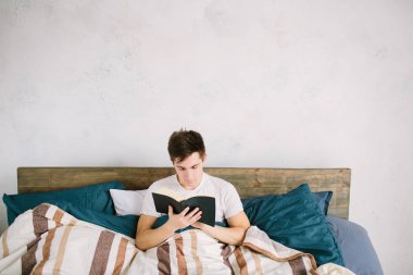 Evdeki yatağında kitap okuyan bir adam.