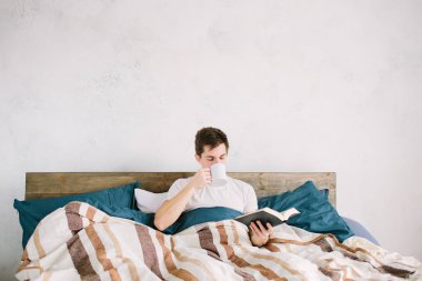 Evdeki yatağında kitap okuyan bir adam.