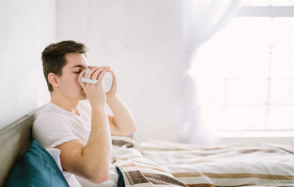 man in bed drinking morning coffee in sunrise light