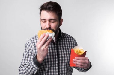 bir parça amburger ve patates kızartması tutan adam. Öğrenci fast food yiyor. yararlı değil gıda. çok aç adam