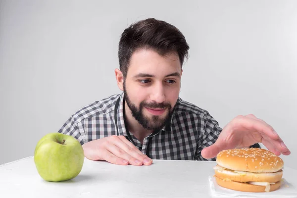 햄버거와 사과 빛 바탕에 체크 무늬 셔츠에 수염된 남자. 사람 사이 신속 하 고 건강 한 음식 선택 하 게. 맛 있는 또는 유용한 딜레마 — 스톡 사진