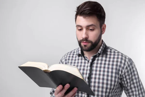 Un uomo con una camicia a scacchi con un libro nero su uno sfondo chiaro. Studente barbuto . — Foto Stock