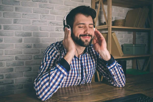 The man is wearing headphones, he sits at home at the computer and listens to music