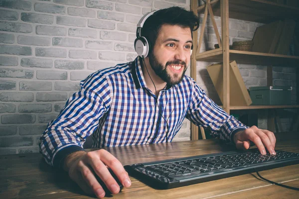 Bearded man playing at home and streaming. Funny guy is excited because of seen virtual video. He is wearing red headphones — Stock Photo, Image