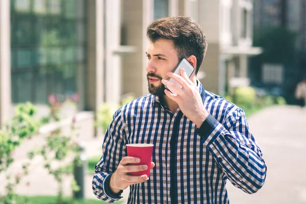 Handsome sporty bearded dark-haired man Drinking coffee and talking on the phone — Stock Photo, Image