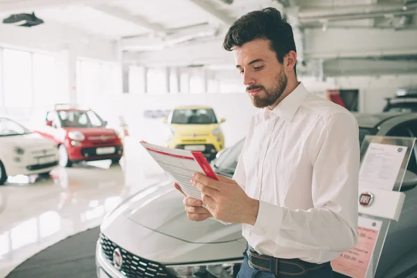 Vendedor de vehículos amigable presentando coches nuevos en la sala de exposición. Foto de un joven consultor masculino mostrando un coche nuevo en el auto show. Concepto de alquiler de coches — Foto de Stock