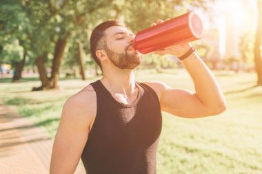 Demir şişe ve içme suyu tutan adam. Genç yakışıklı sportif adam sonra eğitim açık havada dinlenme biçimi. Erkek fitness modeli eğitim egzersiz
