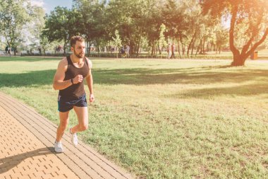 Doğada koşan atletik genç adam. Sağlıklı bir yaşam tarzı. Sakallı siyah saçlı sporcu geri yaktı yolda - günbatımı çalışıyor.