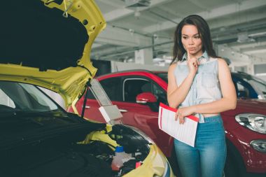 Mükemmel hatları. Genç esmer kadın araba galerisinde incelenmesi ve onun kararı. Genç kadın manken arabada yatay portresi. Bu kazandırır olduğunu düşünüyor