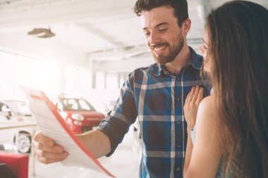 Bir araba showroom satın almak mutlu çift seçer. Güzel genç adam ve kadın otomatik bir araba seçimi göster. Güzel karı koca araba bayilik ayakta ve kendi karar alma