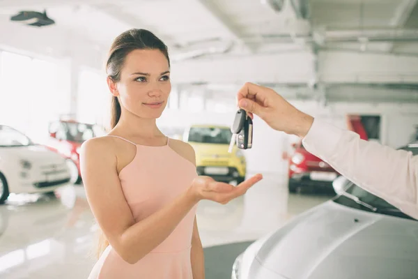 Woman Driver Holding Car Keys. Car Showroom. Seller or car salesman and female client or customer in car dealership presenting the interior decoration of new and used cars in the showroom and hands