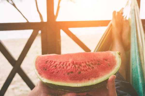 Stilig ung man hålla vattenmelon och ligga i en hängmatta på en solig strand av en ocean — Stockfoto