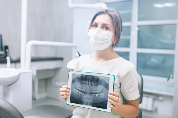 Retrato del dentista femenino. Ella de pie en el consultorio de su dentista y mostrando una radiografía de la mandíbula y los dientes en la tableta PC — Foto de Stock