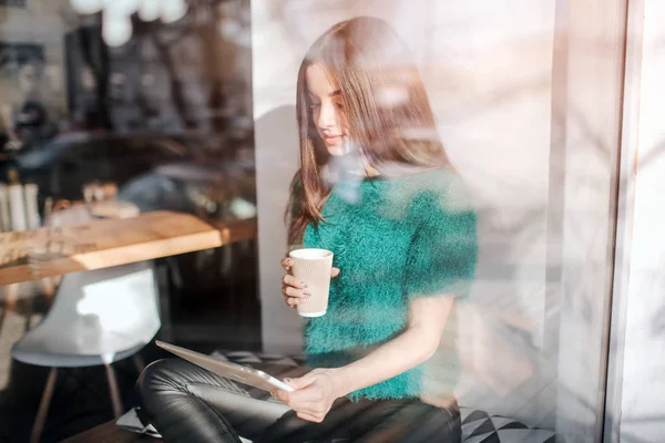 Young beautiful woman drinking coffee at cafe bar. Female model Young using digital tablet at cafe