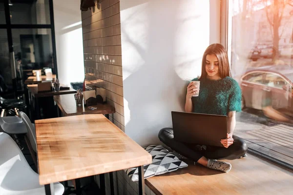 Красива брюнетка використовує ноутбук у кафе. Молода приваблива жінка створює плани на майбутнє, сидячи перед відкритим ноутбуком у затишній кав'ярні . — стокове фото