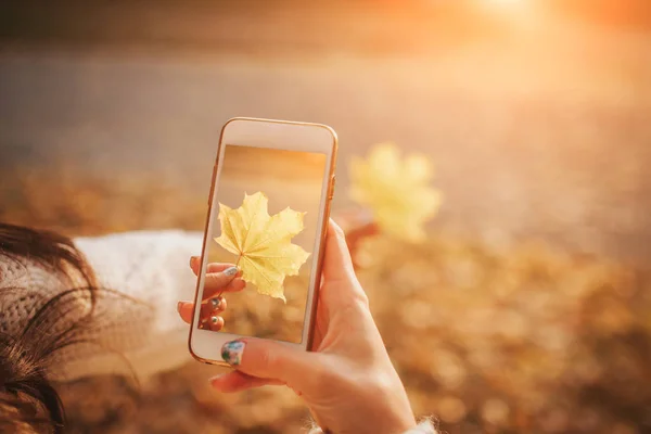 Kobieta za pomocą smartfona w upadku. Jesienna dziewczyna o inteligentny telefon rozmowy w sun flare liści. Portret model Kaukaska w lesie w barwach jesieni. — Zdjęcie stockowe